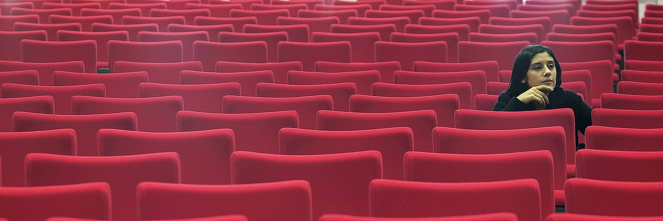 Woman sitting alone in hall of empty red seats 