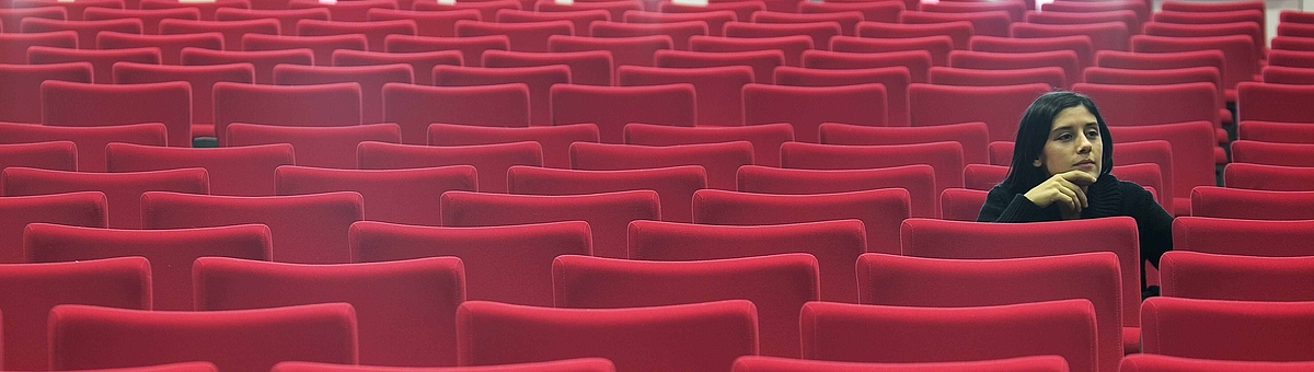 Woman sitting alone in hall of empty red seats 
