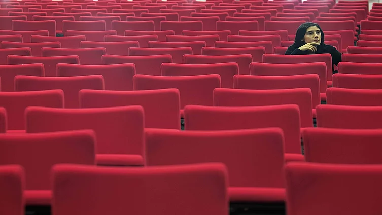 Woman sitting alone in hall of empty red seats 