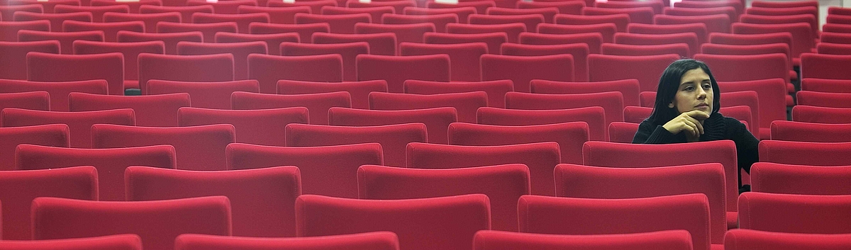 Woman sitting alone in hall of empty red seats 