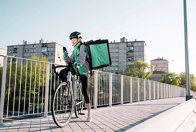 A female delivery worker stopping on a bridge to use her phone