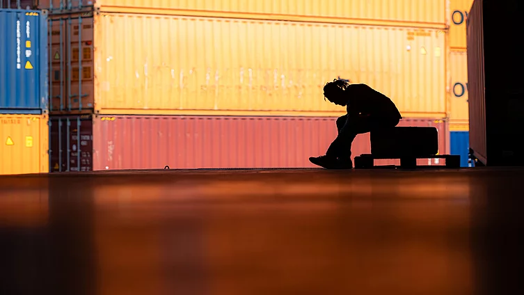 A shadow of a worker sitting alone among containers