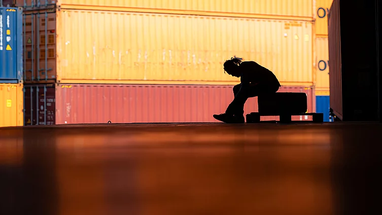 A shadow of a worker sitting alone among containers